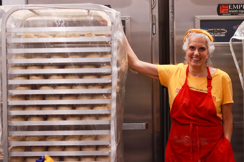 Beth George standing next to a rack of raw bagels at Bagel-ish in Beacon, NY.