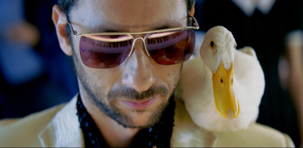 Man with duck on his shoulder and sunglasses on in the film Yes, Directed by Nadav Lapid | Film by Losange