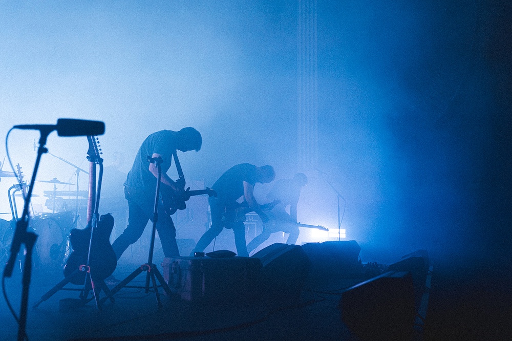 musicians headbanging in unison on stage with blue light by Photographer Brooklyn Zeh