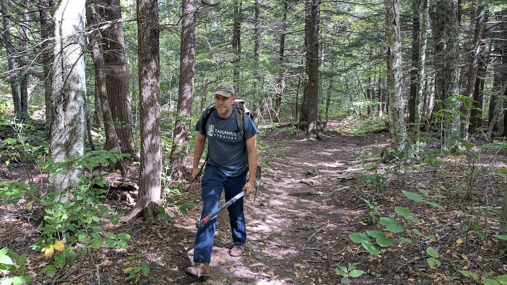 Eddie Walsh hiking up a trail path with gear to a trail he is building in the Catskills