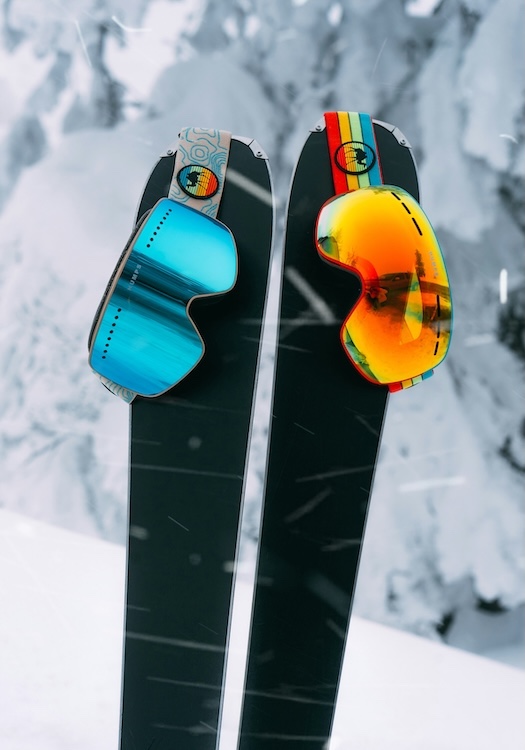 ski goggles with bright reflective colors of blue and orange hanging on skis
