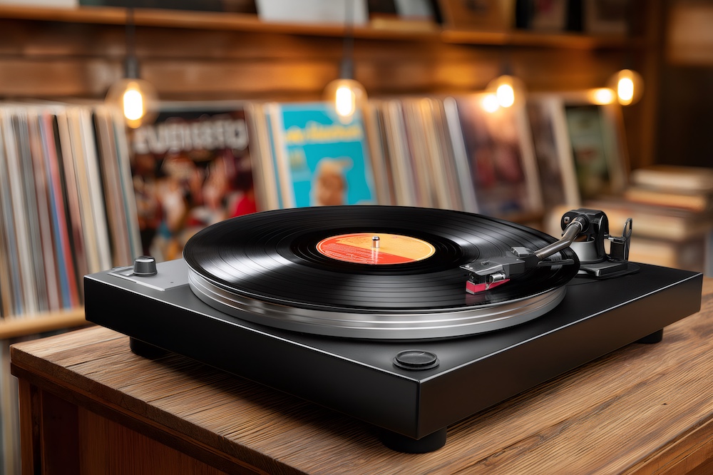 Black turntable playing a vinyl record with warm lighting and a collection of vinyl records in the background, creating a cozy atmosphere