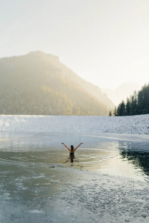 a woman with arms stretched after coming out of being submerged under the water in winter