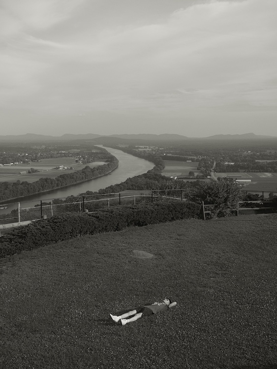 Micky laying on the grass by a river by Ocean Vuong