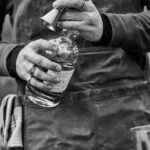 B&W photo of a person with a bottle of Isolation Proof liquor making a cocktail