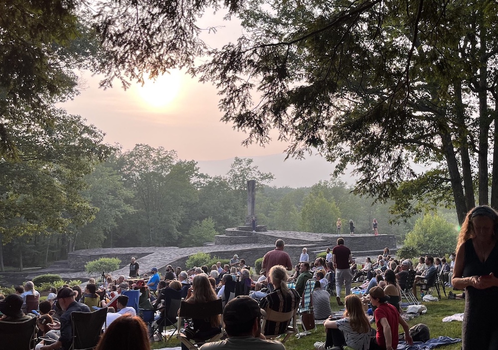 People at Opus 40 watching a concert outside with the the rock sculpture in the background in Saugerties NY