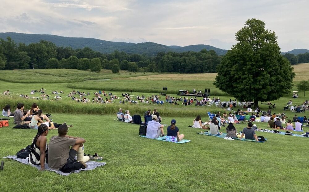 people sitting on blankets all across the fields at Storm King Center while watching a live concert.