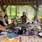 Dan de Lion and Sasha Botanica around a table with other folks of varying ages talking.