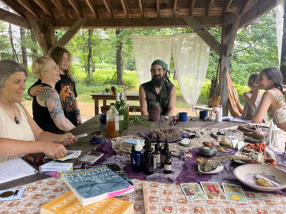Dan de Lion and Sasha Botanica around a table with other folks of varying ages talking.