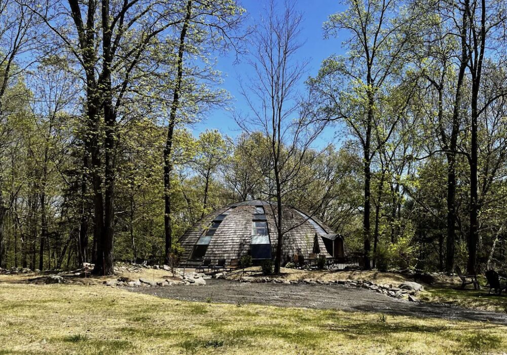 A distance view of a dome house in the woods.