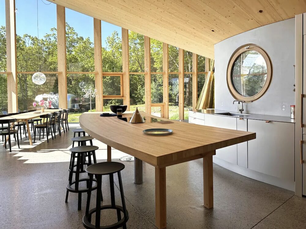 Kitchen table, sink, mirror and a wall of windows in the background.