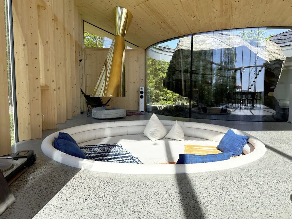 A sunk into the floor living room couch with pillows and brass fireplace hood behind.