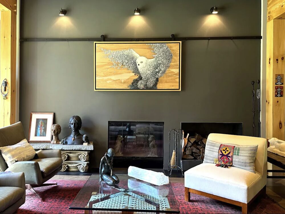 Creative living room with an owl painting, fireplace and sculpture art on side tables next to couch chairs.