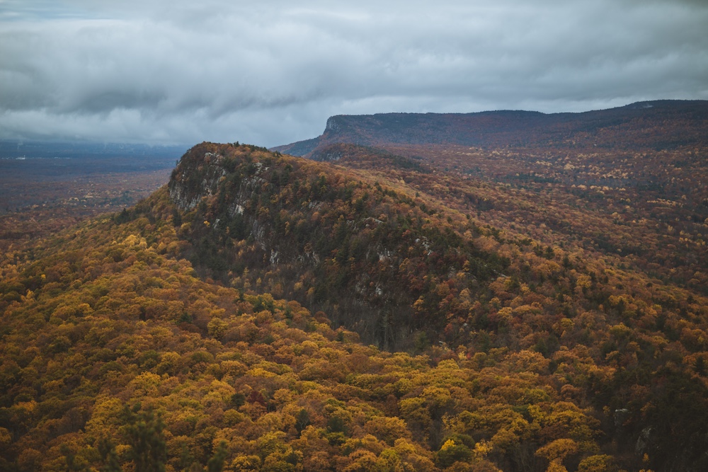 An aerial view of Autumn foliage across Mohonk Mountain Ridge with dark rolling clouds passing over.