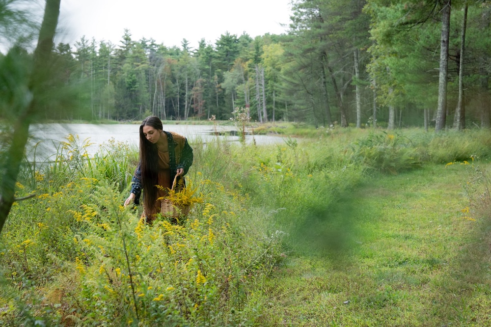 Sasha Botanica foraging herbs in a field next to a pond in the Hudson Valley NY