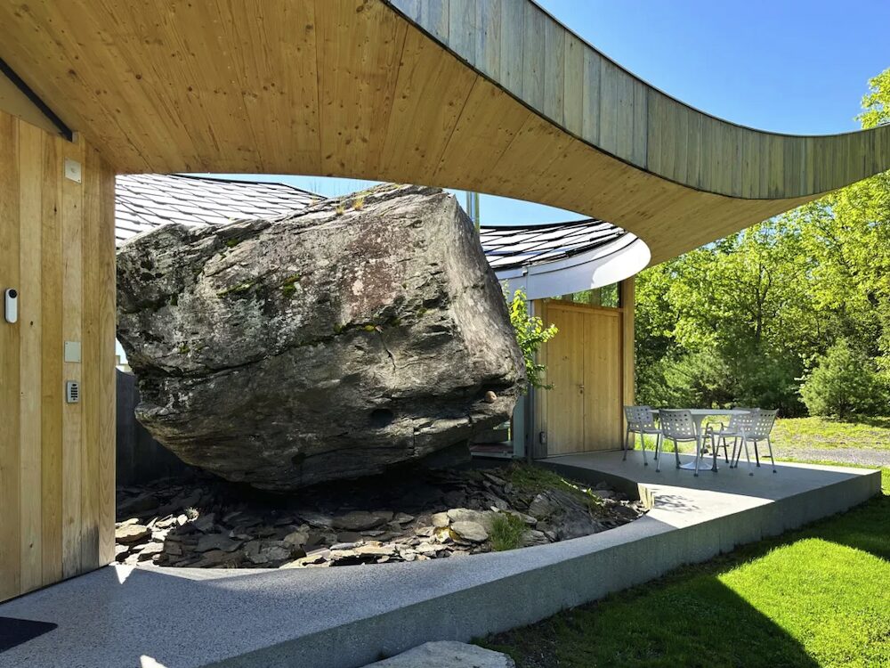 Exterior swooping roof with a hole for a boulder rock and deck built around it.