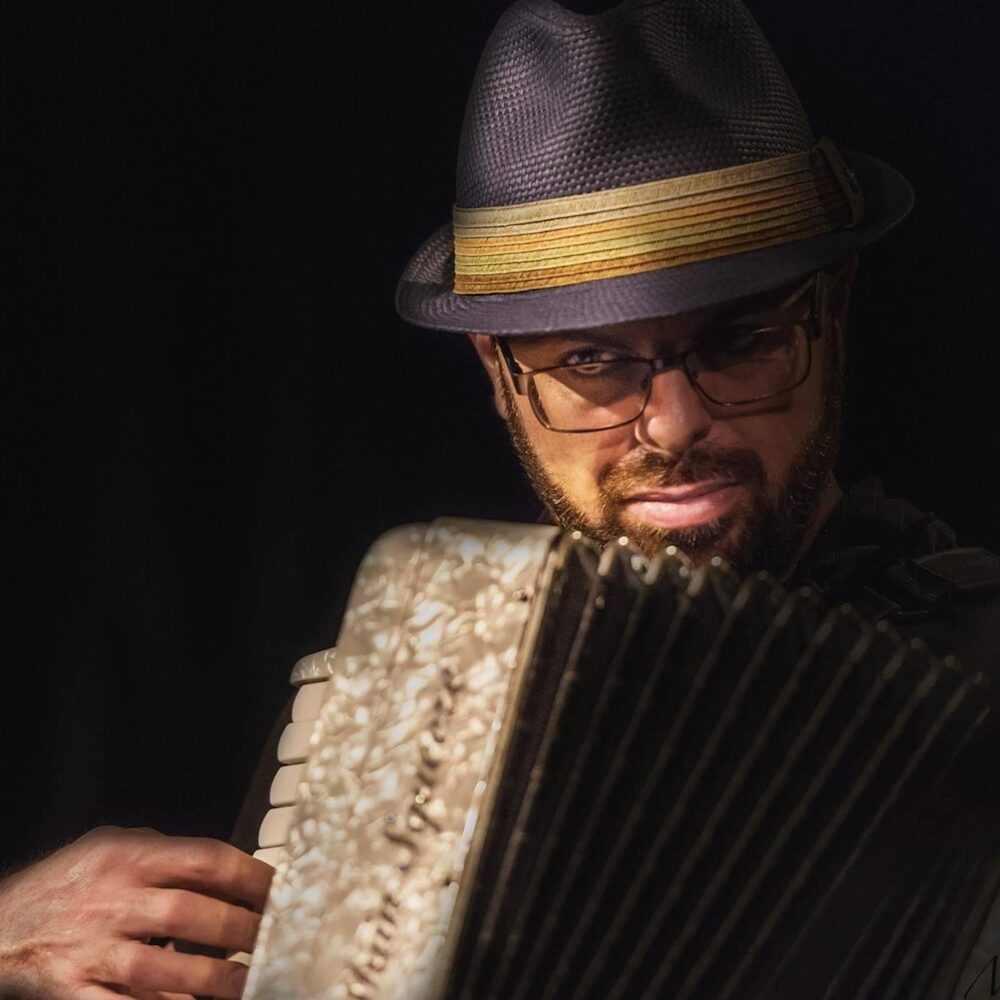 Closeup of Jeremy Baum playing the accordion with a fedora hat on.