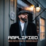Jeremy Baum on the street in front of a venue with "AMPLIFIED" written across the bottom.
