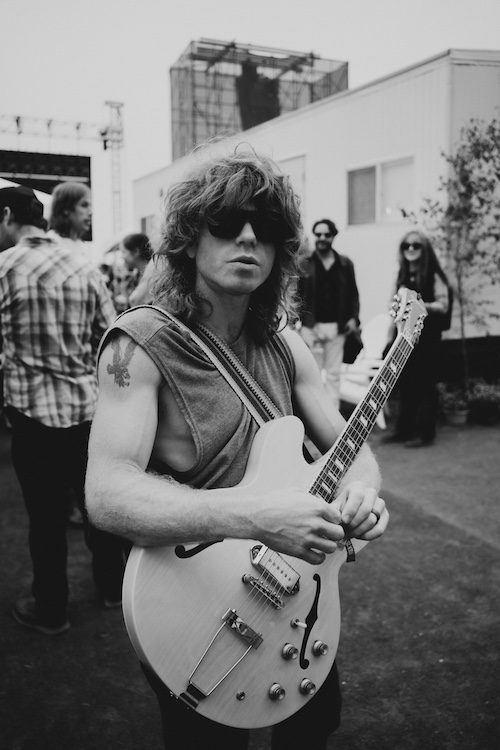 A b&W image of Jesse Wells outside of a show with his guitar.