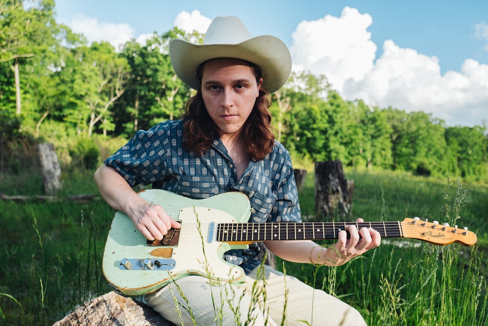 Daniel Donato playing electric guitar in the country with a white cowboy hat on.