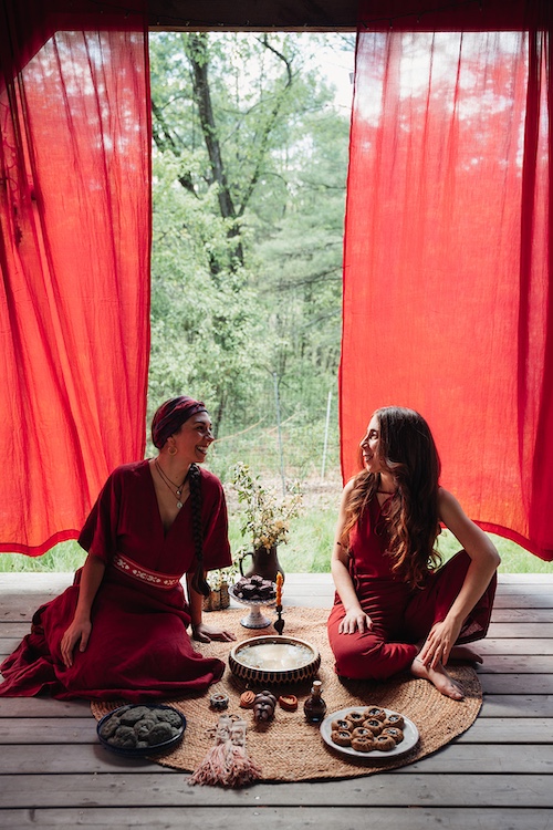Sasha Botanica and Diana Wassef sitting under the red curtains in nature.