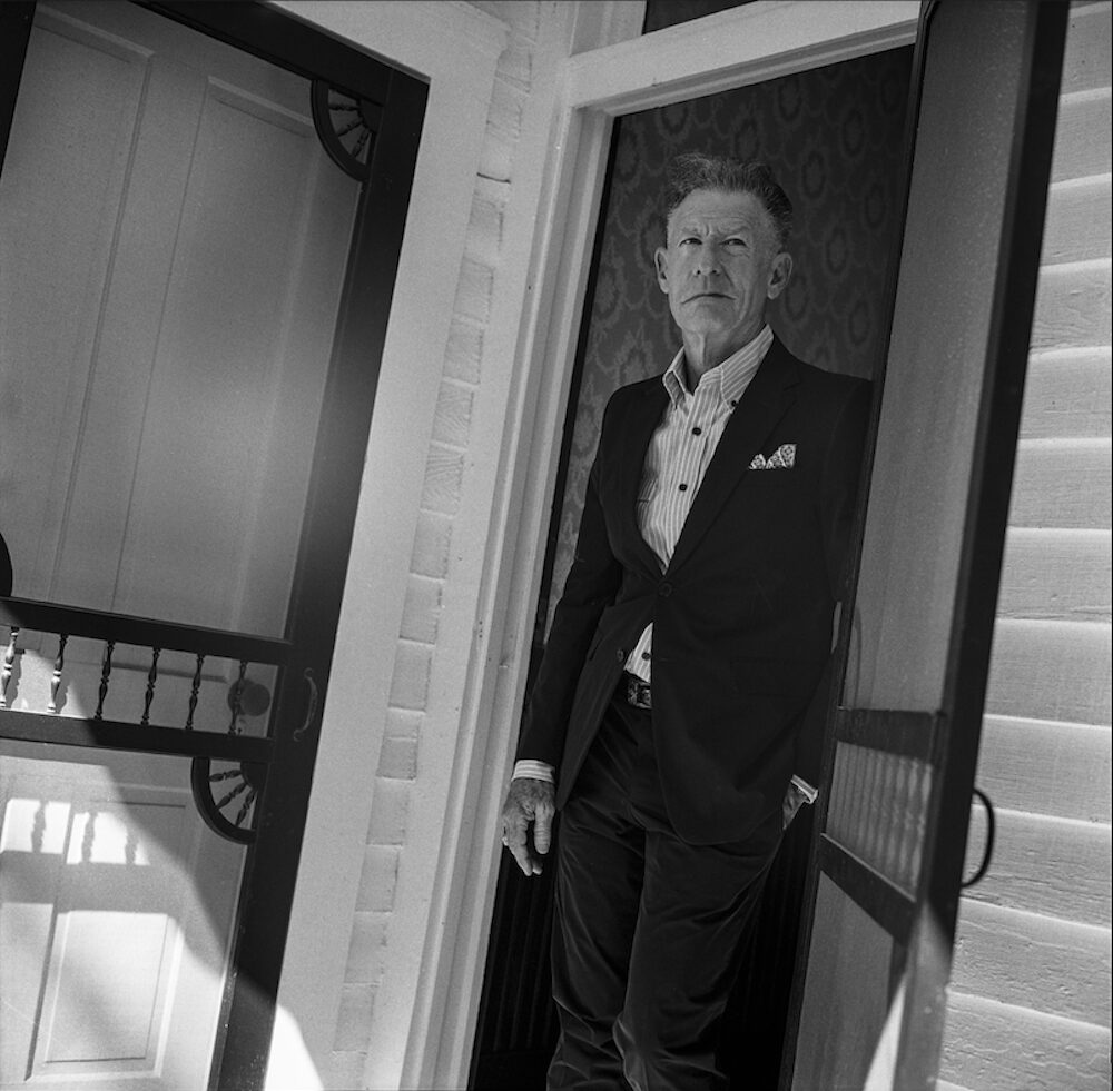 Lyle Lovett standing in the doorway of a house.