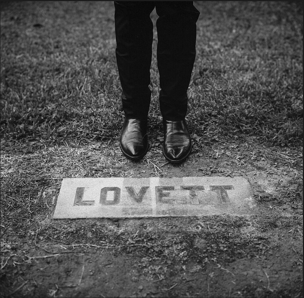 Lyle Lovett's boots pointing towards a door mat with his name on it.