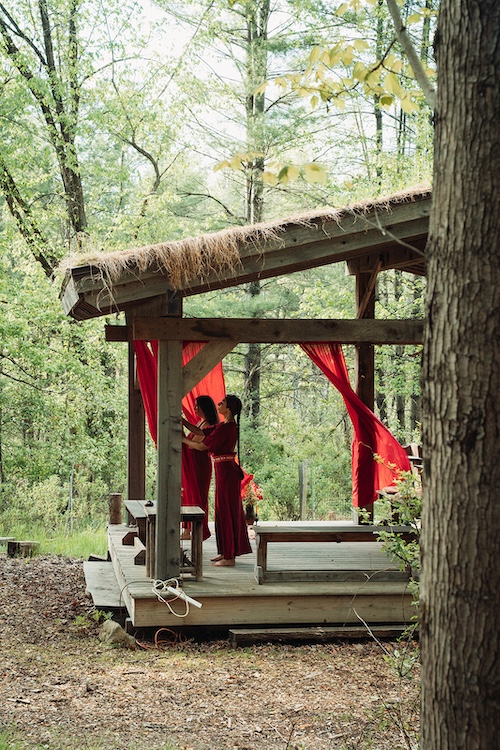 A distance shot of Sasha Botanica and Diana Wassef in the lento with red curtains blowing in the wind.