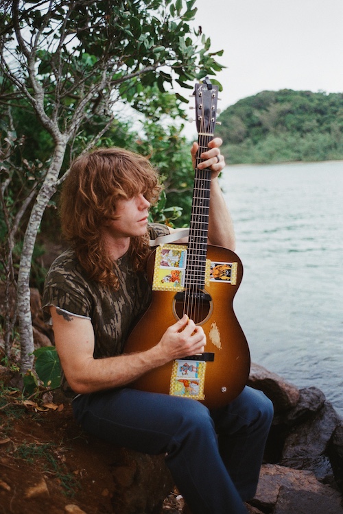 Jesse Wells sitting by the river with his guitar.