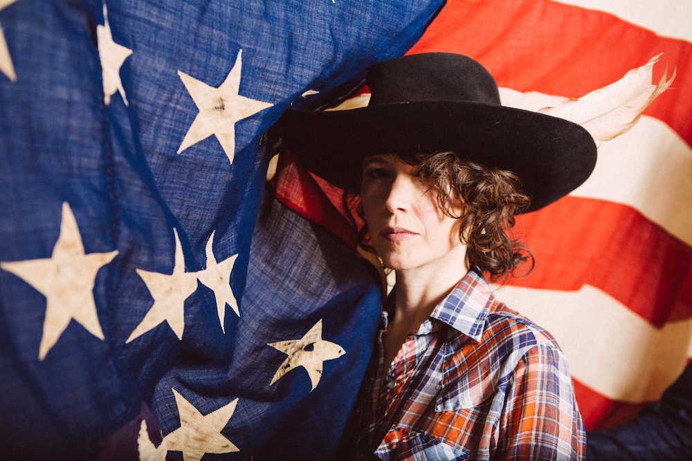 Sarah Lee Guthrie with a black hat in front of the American Flag.
