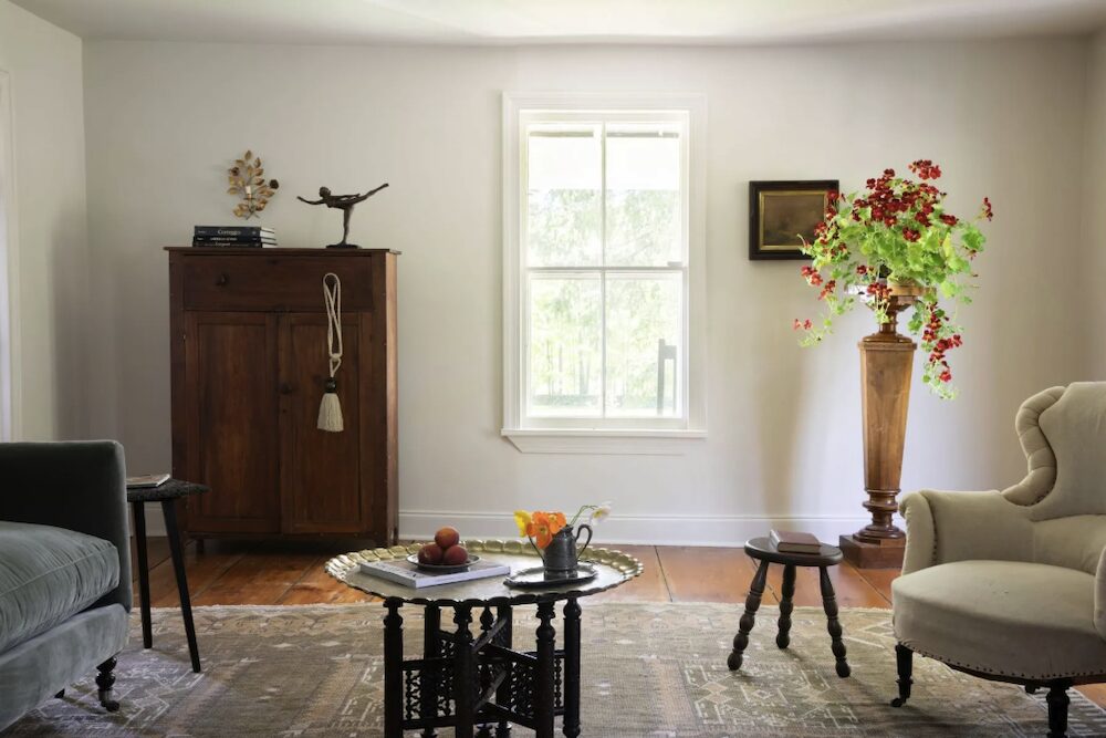 The sitting room with couch, chairs, vase and flowers and drawers by the window of the kitchen sink at 809 North Quaker Hill Road, Pawling NY.