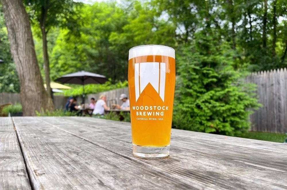 A blonde beer in a glass with log on a picnic table outside at Woodstock Brewery in Mount Tremper NY.