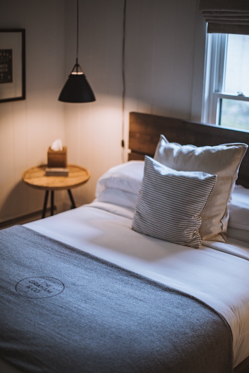 A made bed with lit lamp Interior of a guest room at the Graham & Co hotel in Phoenicia, NY.