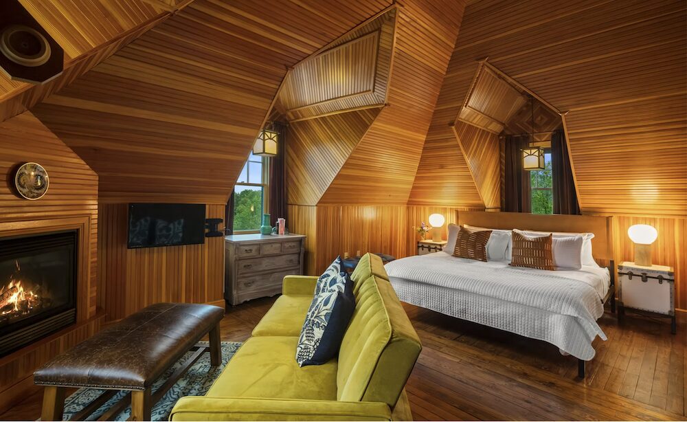 A bedroom filled with wooden ceiling and walls, bed, couch and fireplace at Hotel Mountain Brook in Tannersville NY.