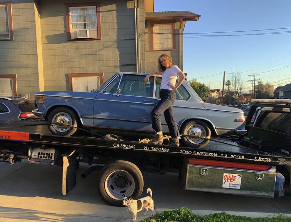 Fiona Dourif posing halfway in the door of a blue BMW on a car bed.