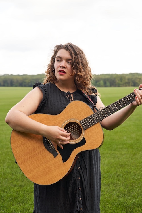 Xondra singing in a field with her guitar.