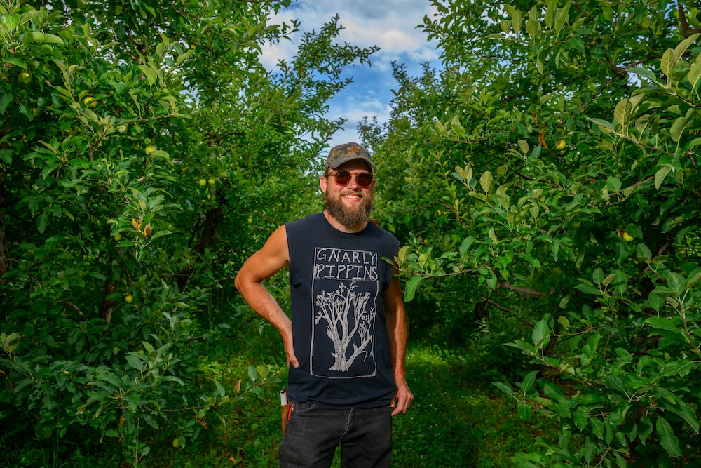 Orchardist, Kevin Clark, smiling between the trees at Rose Hill Farm in Red Hook NY.