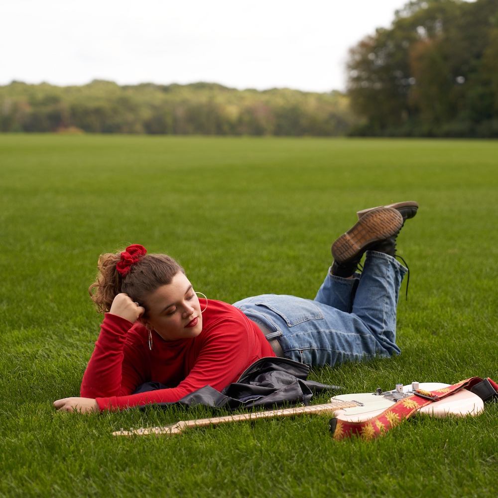 Xondra laying on her stomach next to her guitar.