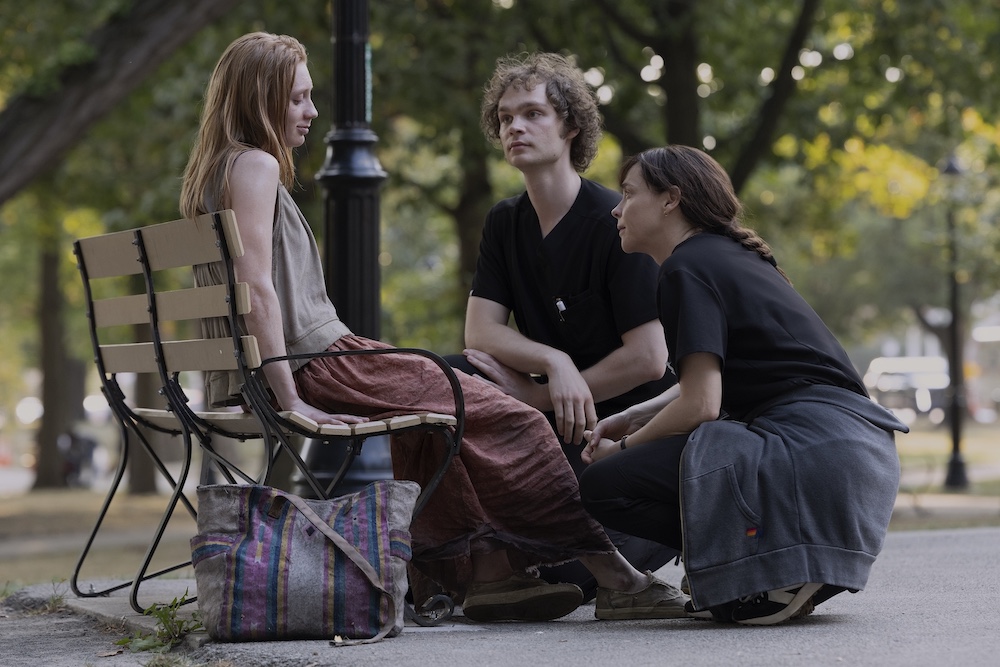 Fiona Dourif and another young doctor heloing a women on a bench in a park on the TV show, The Pitt.