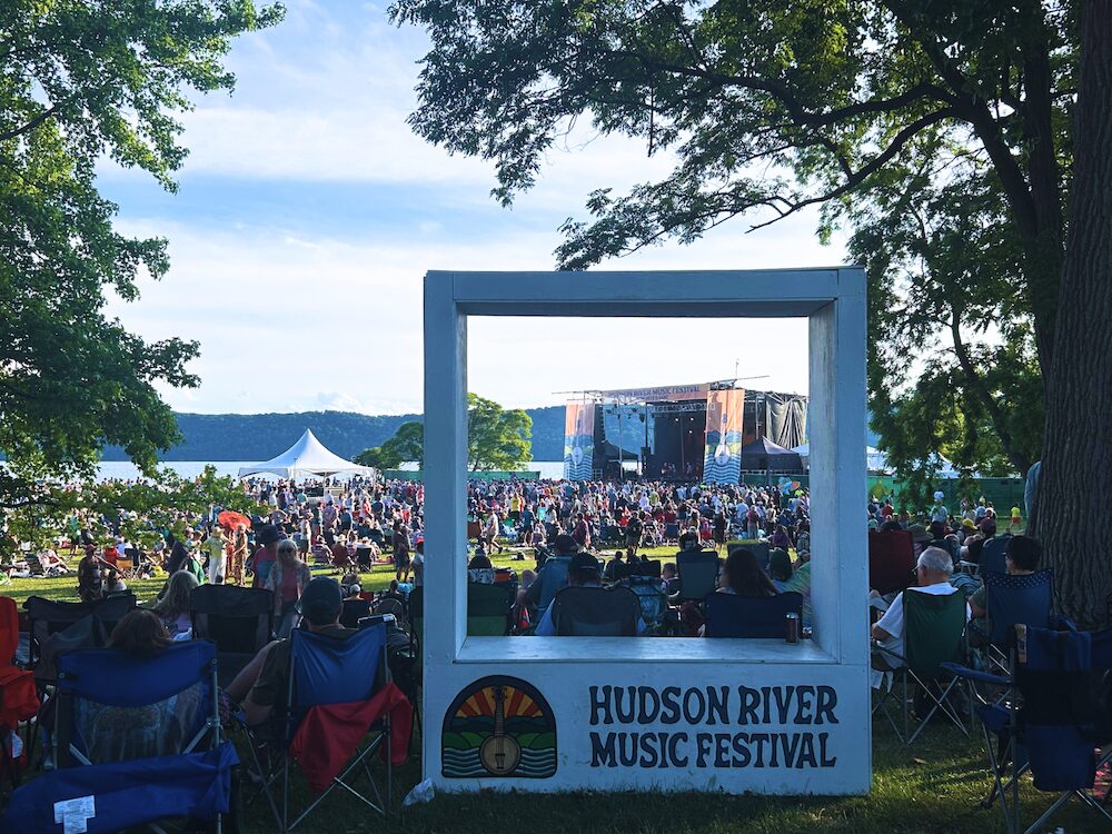 View from the top of the hill of the main stage, crowd and Hudson River at Hudson River Music Festival at Croton Point Park NY.