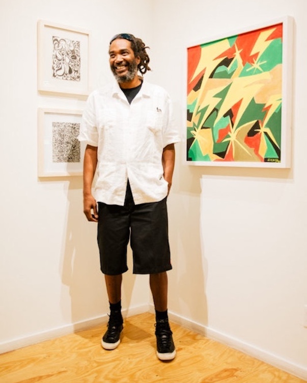 Darryl Jenifer in a gallery standing next to art on the walls.