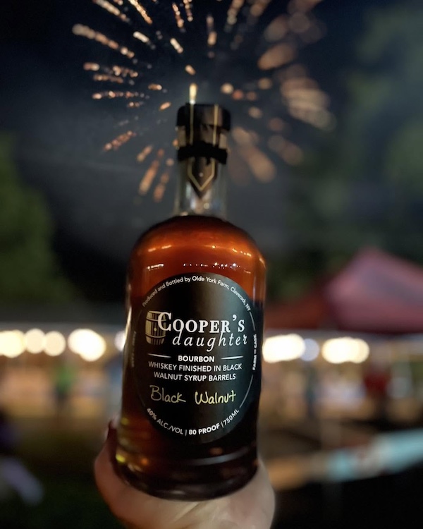 Black Walnut spirits in a bottle with fireworks in the background at Cooper's Daughter Spirits in Claverack, NY.