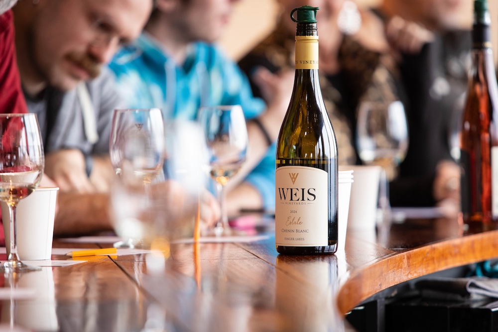 A bottle of wine on the counter with people all around at Weis Vineyards in Hammondsport NY.